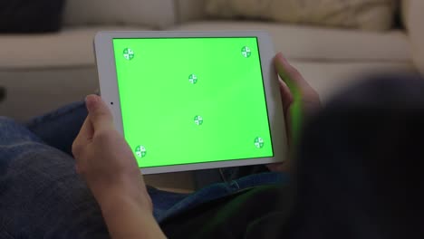 hombre joven sentado en el sofá, adolescente masculino en casa usando un dispositivo móvil para la tarea. tableta monitor de computadora pantalla verde para internet.