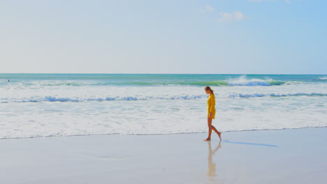 Side-view-of-young-Cuacasian-woman-splashing-water-on-beach-while-walking-on-the-beach-4k