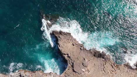 aerial, tilt up, drone shot of waves hitting a rocky coast, blue sea, on a sunny day, in mallorca, spain