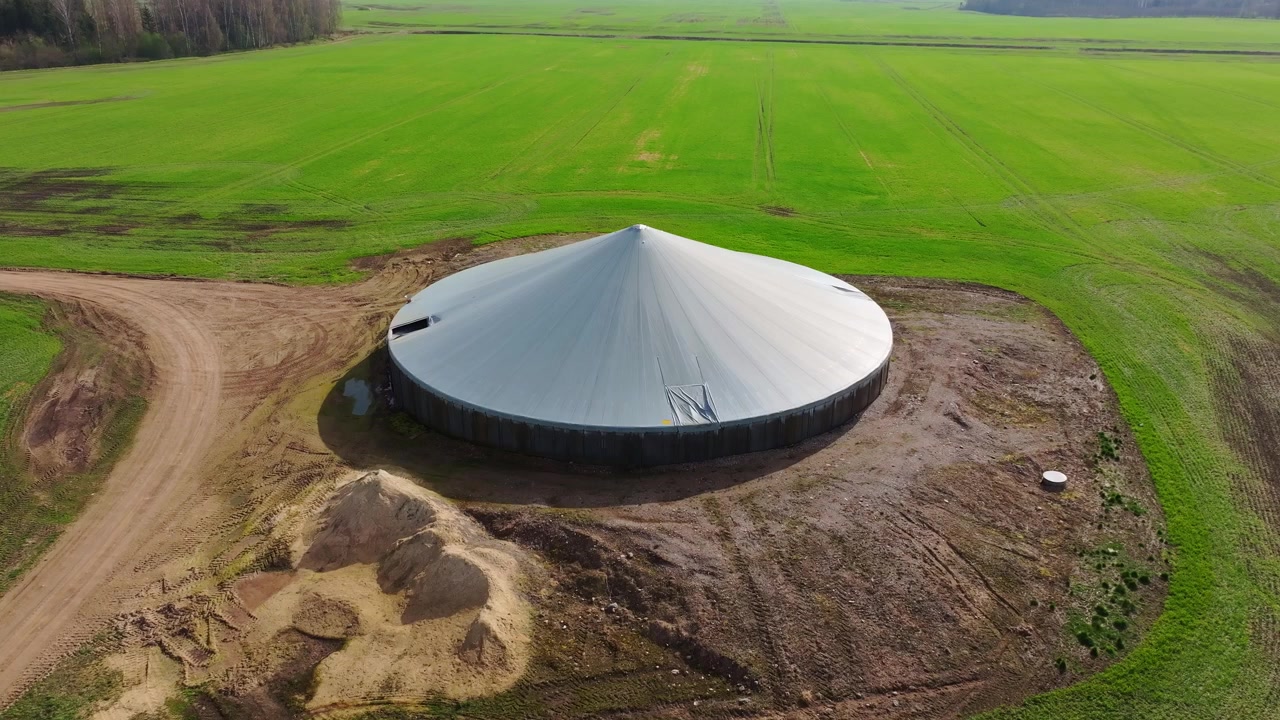 Un drone orbita attorno a un serbatoio agricolo coperto circondato da campi coltivati primaverili di un verde vivido.