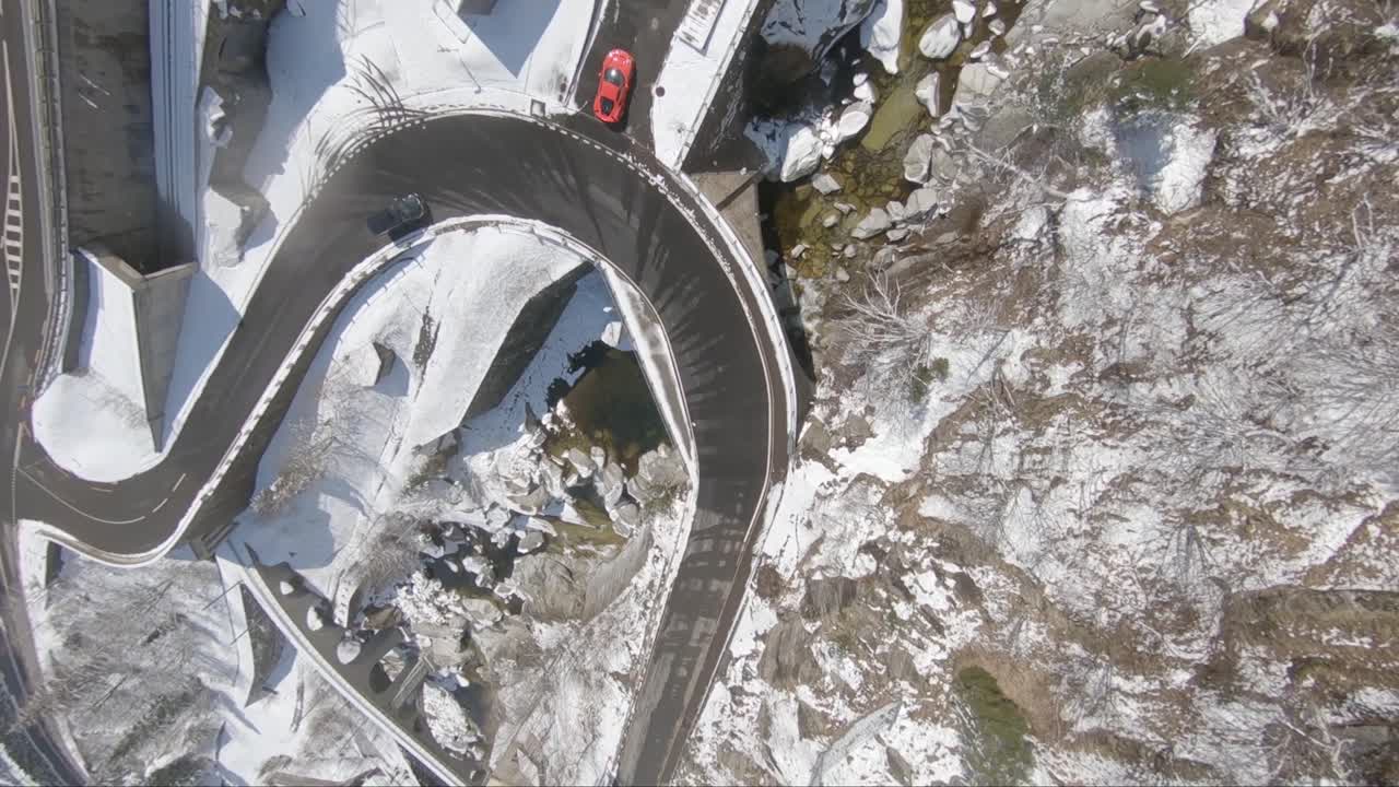Twist and roll of a high speed racing drone on a mountain road with a parked red car below