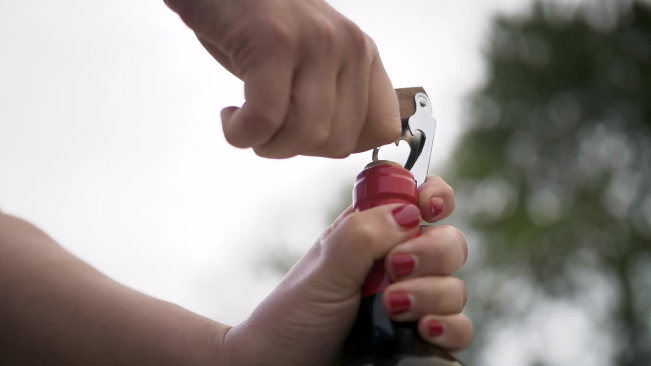 abrir una botella de vino rojo al aire libre con dos manos y un tornillo de corcho