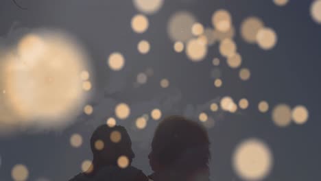 Animation-of-light-spots-over-african-american-couple-at-beach