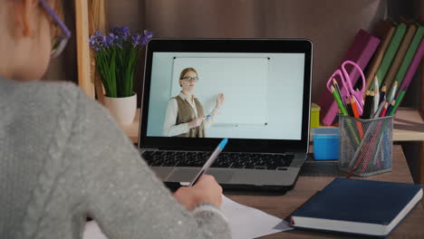 girl learns at home online with her laptop while her teacher tells lesson on screen