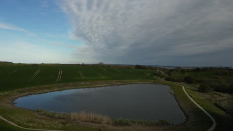 Footage-of-a-lake-by-a-field,-recorded-by-a-drone-flying-over-the-lake