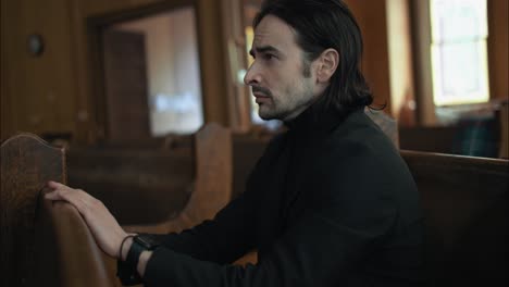 Young-man-in-black-suit-sitting-in-pew-in-church-praying-in-worship-in-cinematic-slow-motion