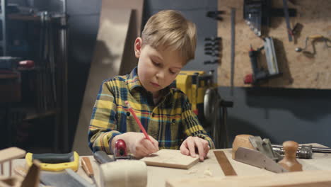 caucasian little cute boy working in carpentry workshop and drawing with pencil