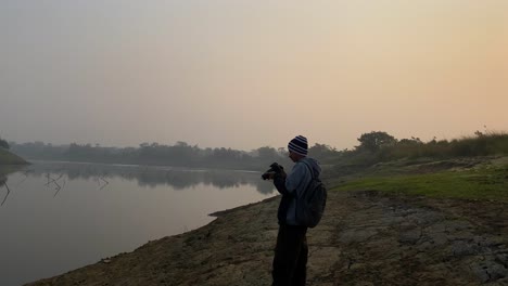 young photographer with hat takes pictures of polluted river in sylhet, dolly in
