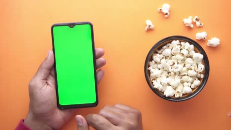 hombre de mano usando teléfono inteligente y comiendo palomitas de maíz