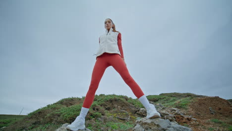 fitness lady training muscles on grassy rocky hills cloudy day. motivated woman