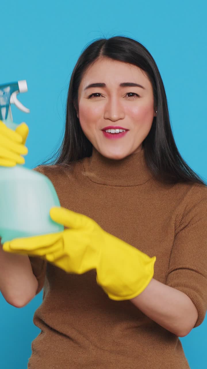 Video verticale: sorridente collaboratrice domestica asiatica che indossa guanti protettivi mentre mostra uno spray detergente chimico davanti alla telecamera