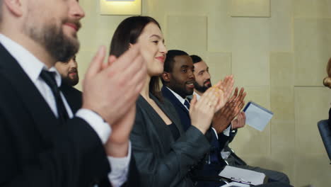 close-up view of multiethnic business people sitting on chairs and clapping in a conference room