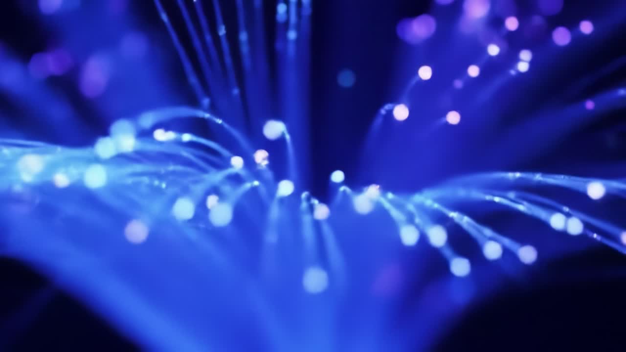 In a dark setting, vibrant blue fiber optic lights pulse and twinkle, creating a mesmerizing display. The scene captivates with glowing strands that resemble a flowing underwater landscape.