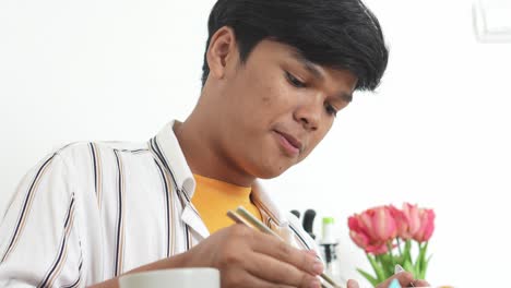 Low-Angle-View-Of-Young-Asian-Man-Eating-Delicious-Instant-Noodle-Using-Chopstick-At-Home-With-Happy-Expression