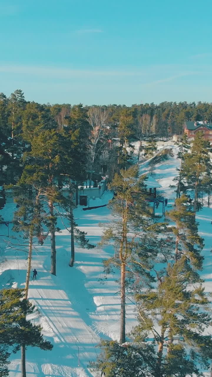 popular ski resort with buildings and tracks on snowy hills in evergreen wood on sunny winter day upper view