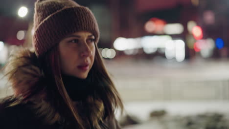 first-person view of a woman in a winter coat with a fur hood, walking on a road at night. the cold air is visibly coming out of her mouth, and the background features blurry city lights