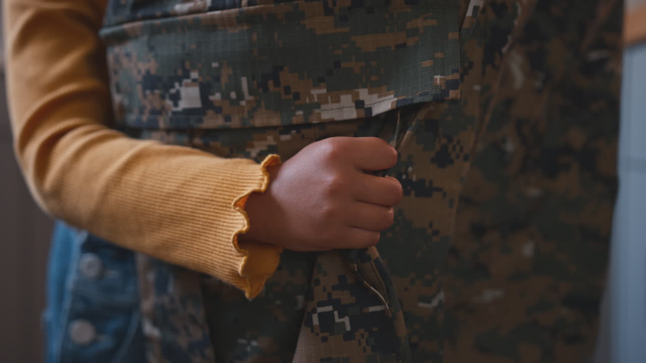 primer plano de la hija abrazando las piernas del padre del ejército en uniforme en casa de licencia en la cocina de la familia
