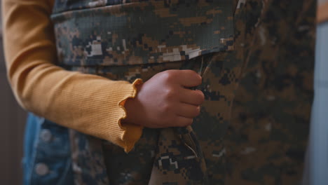 primer plano de la hija abrazando las piernas del padre del ejército en uniforme en casa de licencia en la cocina de la familia