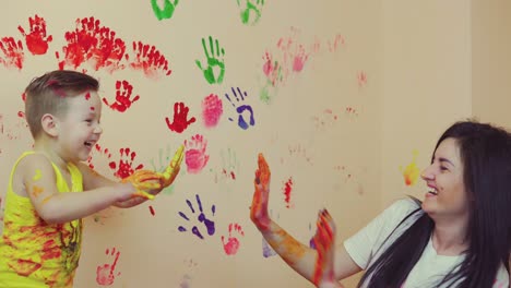 Glückliche-Mutter-Und-Ihr-Süßer-Junge-Haben-Spaß-Zusammen-Und-Hinterlassen-Ihre-Bunten-Handabdrücke-An-Der-Wand.-Junge-Glückliche-Familie.-Mutter-Kind-Konzept