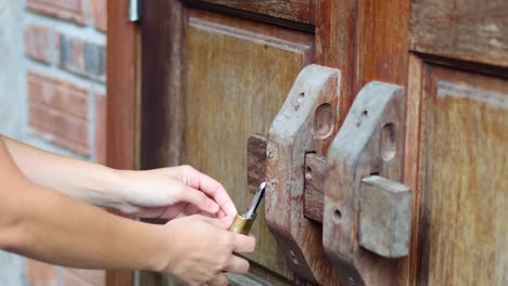 hands unlocking an old padlock on a wooden door