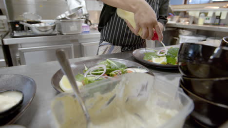 close up of chef's hand putting cream on salad