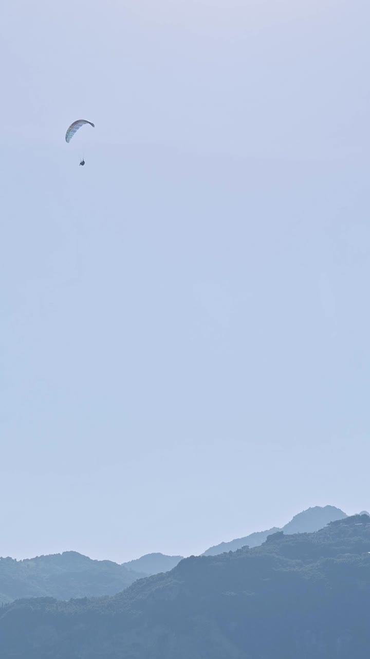 Paraglider pilot slowly descending over blue hazy mountains
