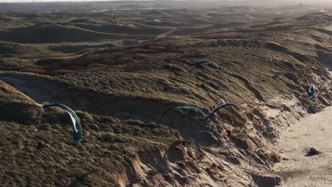 Golden-hour-light-casts-on-extreme-sports-paragliders-soaring-above-sand-dune-slopes-of-Castricum-beach,-Netherlands