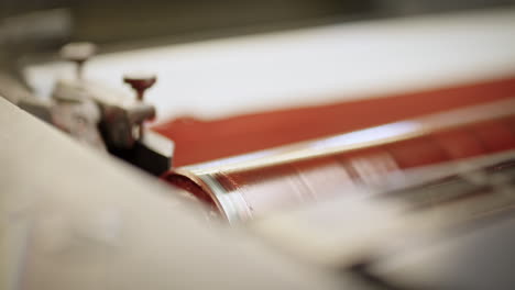 Printing-roller-turning-on-the-machine-covered-in-light-red-color,-close-up