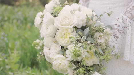 close up of bride in her lace wedding gown holding bouquet of white roses and greenery in her hands outdoors 1080p 60fps