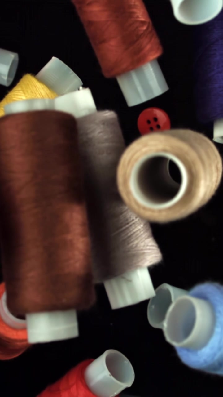 Red Button Dropping onto Colorful Sewing Thread Spools