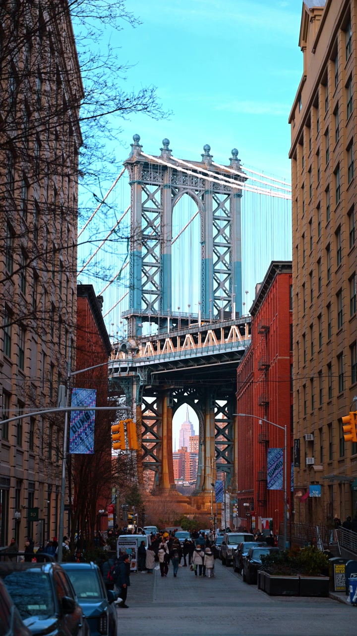 New York, USA, 11 maggio 2026: Ponte di Manhattan incorniciato da edifici in mattoni a Brooklyn. Vista di Washington Street con pedoni, semaforo e Empire State Building visibile attraverso la struttura del ponte