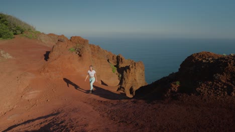 Woman-hiking-through-unique-orange-coastal-landscape-with-view-of-ocean