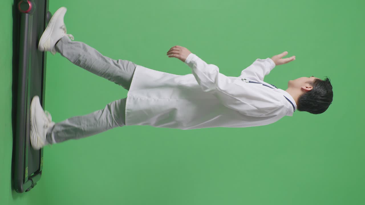 병원에서 녹색 스크린 배경에서 는 동안 스테토스코프를 들고 손을 흔들고 미소 짓는 아시아 남성 의사