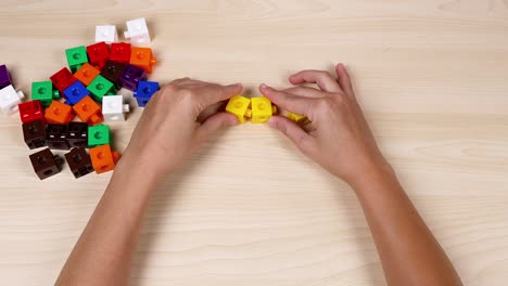 hands assembling yellow cubes on a wooden table