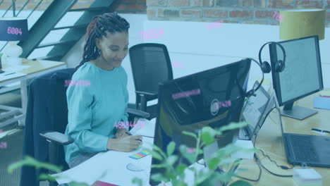 animation of changing numbers, african american woman looking at computer and writing in notepad