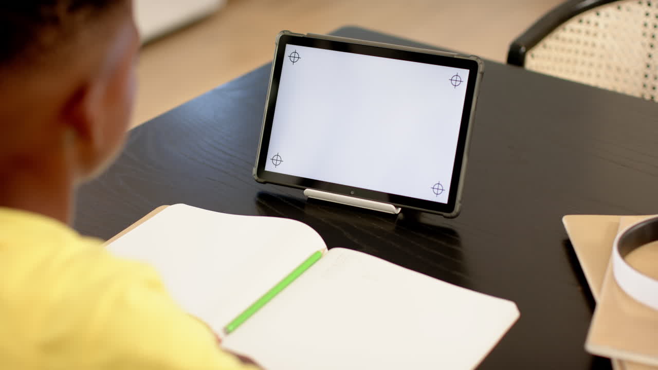 Using tablet and writing in notebook, student studying at school desk, copy space