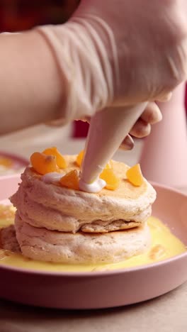 preparing a stacked pancake dessert with whipped cream and mandarin orange