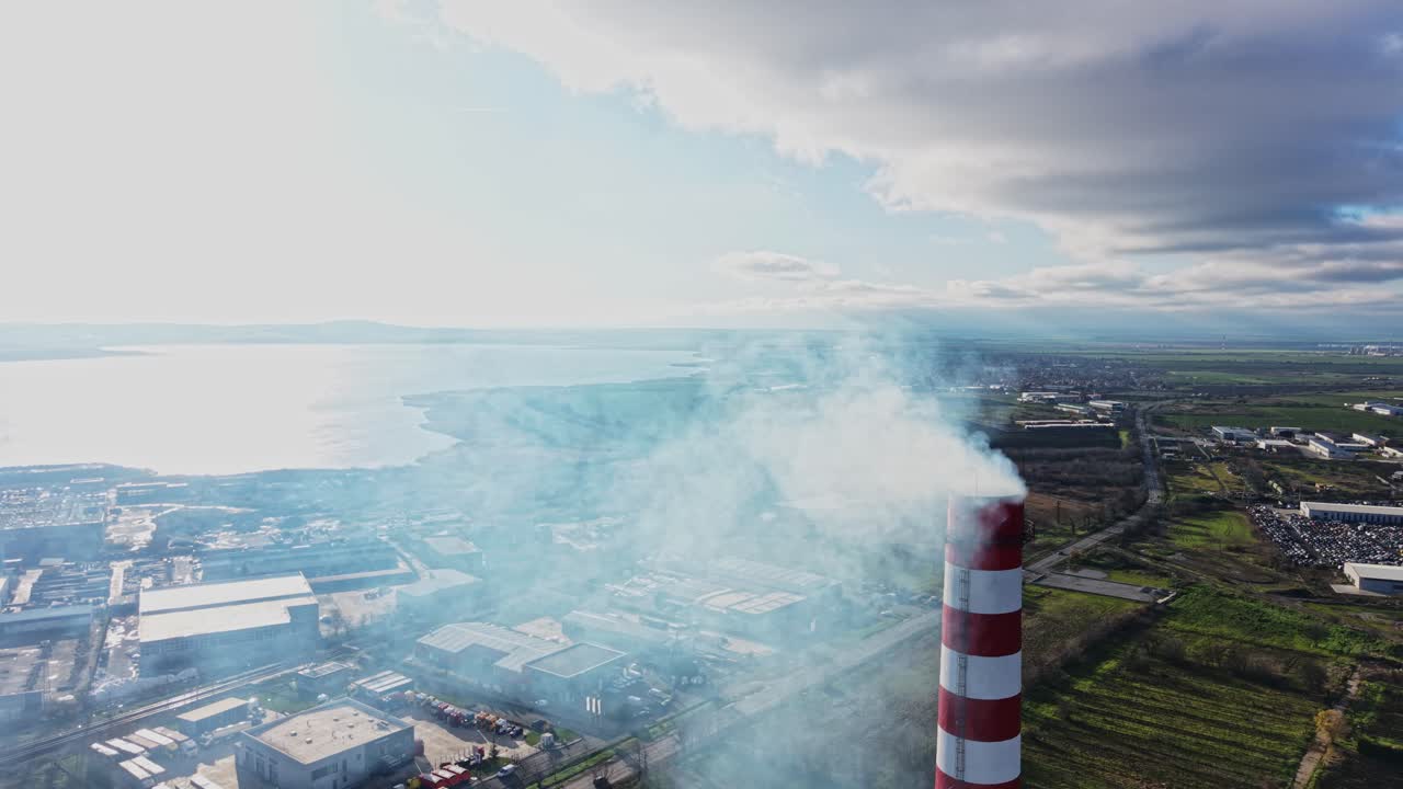 Fumo che si alza da un camino industriale vicino all'acqua e ai campi durante il giorno