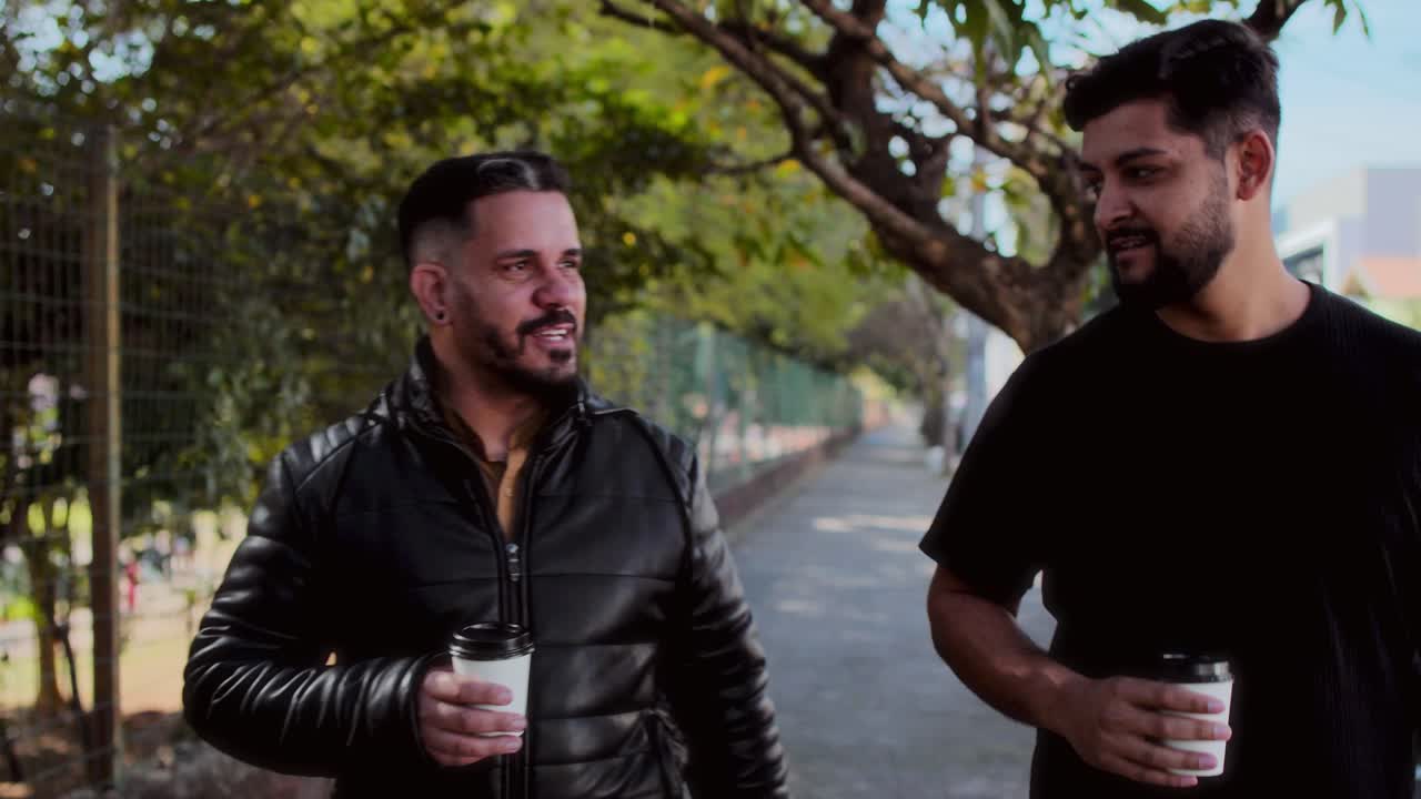 Two men walking and talking outdoors while holding coffee cups