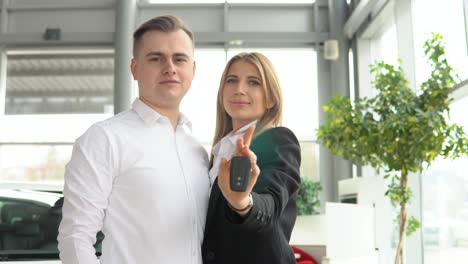 pareja feliz mostrando las llaves de su nuevo coche en el concesionario. negocio de automóviles, venta de automóviles