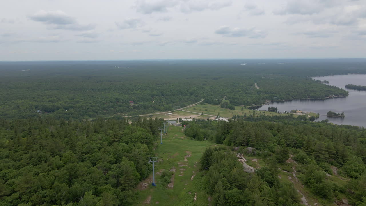 Aerial shot over green tree covered mountain with lake along coast. Calabogie ski hill. Ontario Canada