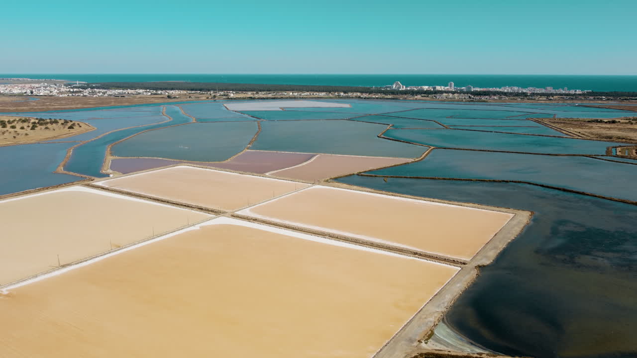 Aerial flyover colorful salt lakes in Portugal with Atlantic Ocean in background - Europe during summer day