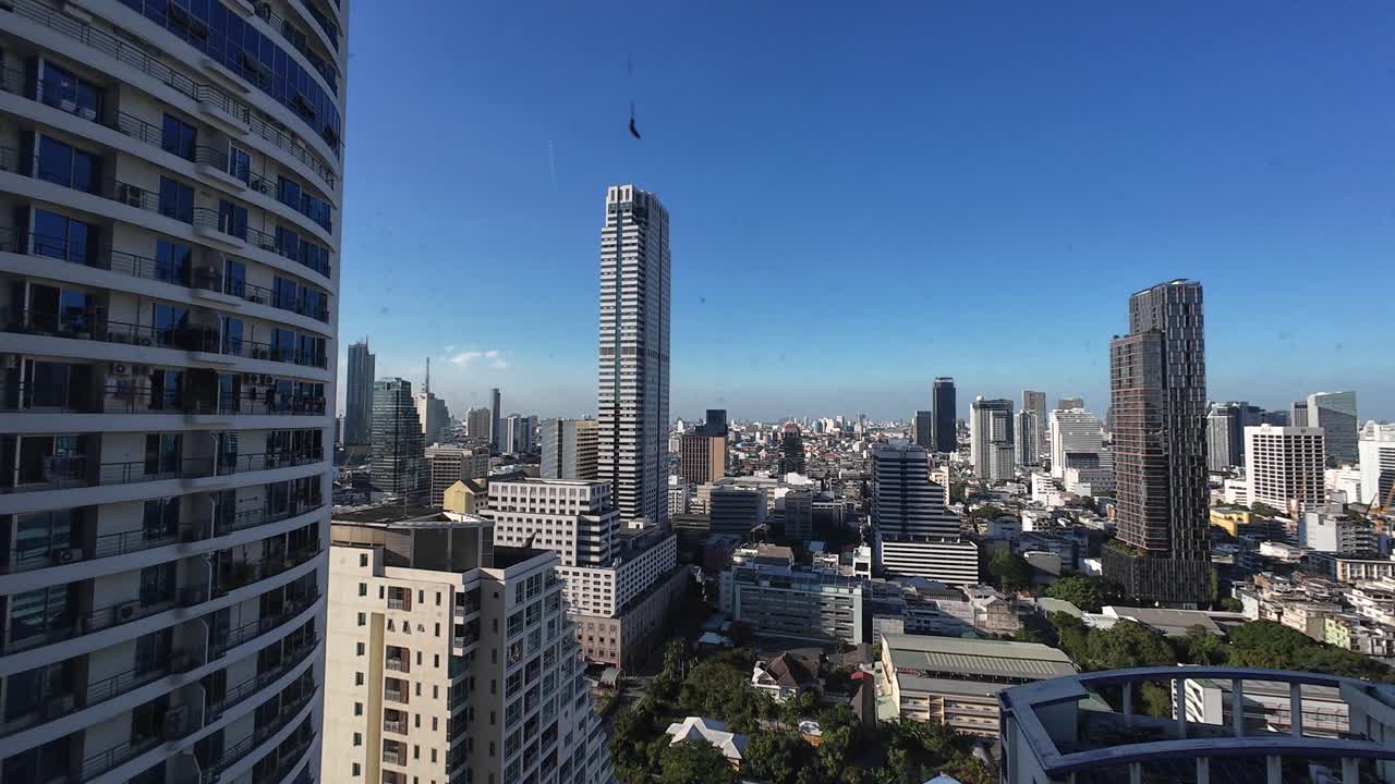 Ripresa panoramica che mostra lo skyline della città di Bangkok da un balcone di un grattacielo con edifici moderni, cielo blu chiaro, paesaggio urbano, prospettiva di viaggio, atmosfera cittadina tranquilla diurna.