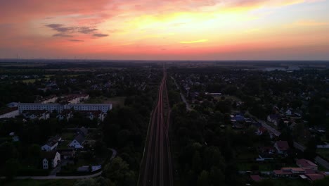 passenger train traveling on a railroad through a small village and forest at dusk. stunning aerial view flight overflight flyover drone