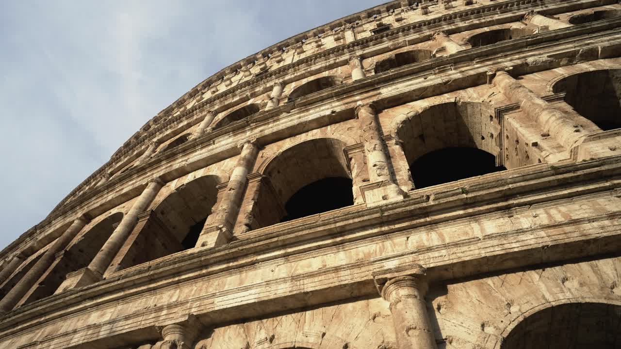 콜로세움 옆에서 카메라를 위로 기울이고 옆으로 걸어가는 동안 이탈리아 로마에서 4k로 새 두 마리가 날아갑니다.