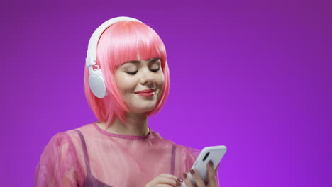 beautiful woman wearing a pink wig and big headphones with smartphone in hands dancing and laughing