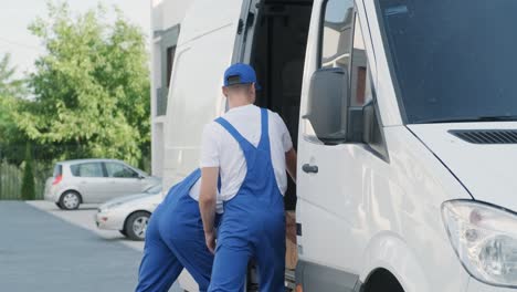 dos jóvenes trabajadores de una compañía de mudanzas están cargando cajas y muebles en un minibus