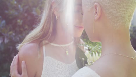 feliz pareja de mujeres diversas sosteniendo un ramo de flores y abrazándose en el jardín