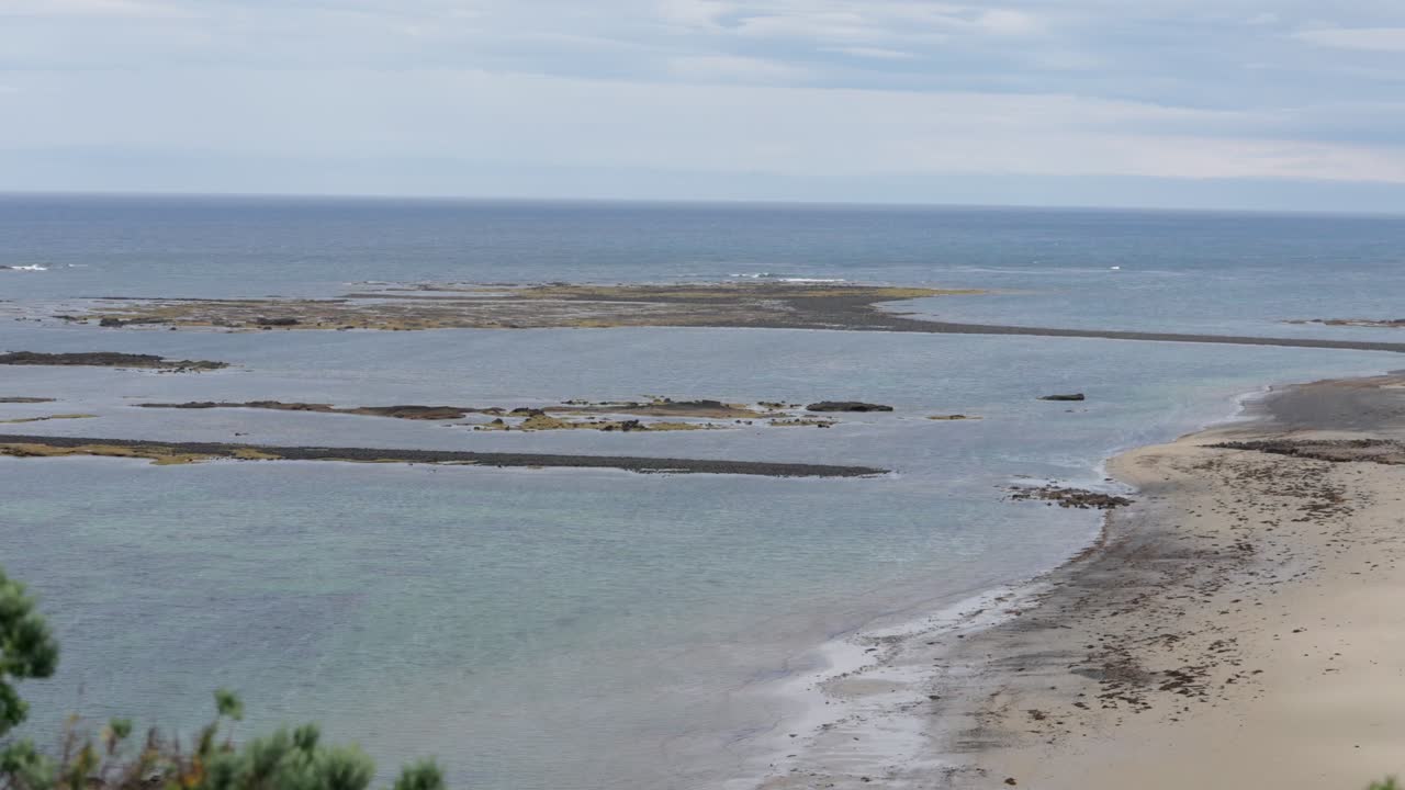 A scenic walkway leads to a rocky island surrounded by calm waters, offering stunning coastal views and a peaceful atmosphere under a clear sky.