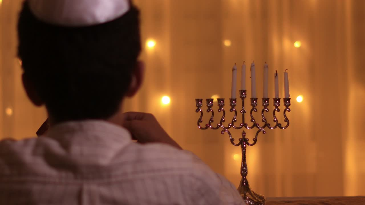 rear view jewish boy lights fifth menorah candle during jewish holiday Hanukkah